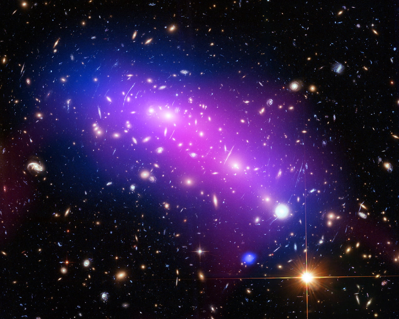 At first glance, this cosmic kaleidoscope of purple, blue and pink offers a strikingly beautiful — and serene — snapshot of the cosmos. However, this multi-coloured haze actually marks the site of two colliding galaxy clusters, forming a single object known as MACS J0416.1-2403 (or MACS J0416 for short). MACS J0416 is located about 4.3 billion light-years from Earth, in the constellation of Eridanus. This new image of the cluster combines data from three different telescopes: the NASA/ESA Hubble Space Telescope (showing the galaxies and stars), the NASA Chandra X-ray Observatory (diffuse emission in blue), and the NRAO Jansky Very Large Array (diffuse emission in pink). Each telescope shows a different element of the cluster, allowing astronomers to study MACS J0416 in detail. As with all galaxy clusters, MACS J0416 contains a significant amount of dark matter, which leaves a detectable imprint in visible light by distorting the images of background galaxies. In this image, this dark matter appears to align well with the blue-hued hot gas, suggesting that the two clusters have not yet collided; if the clusters had already smashed into one another, the dark matter and gas would have separated. MACS J0416 also contains other features — such as a compact core of hot gas — that would likely have been disrupted had a collision already occurred. Together with five other galaxy clusters, MACS J0416 is playing a leading role in the Hubble Frontier Fields programme, for which this data was obtained. Owing to its huge mass, the cluster is in fact bending the light of background objects, acting as a magnifying lens. Astronomers can use this phenomenon to find galaxies that existed only hundreds of million years after the big bang. For more information on both Frontier Fields and the phenomenon of gravitational lensing, see Hubblecast 90: The final frontier. Links  Hubblecast 90: The final      frontier Link to Hubblesite release